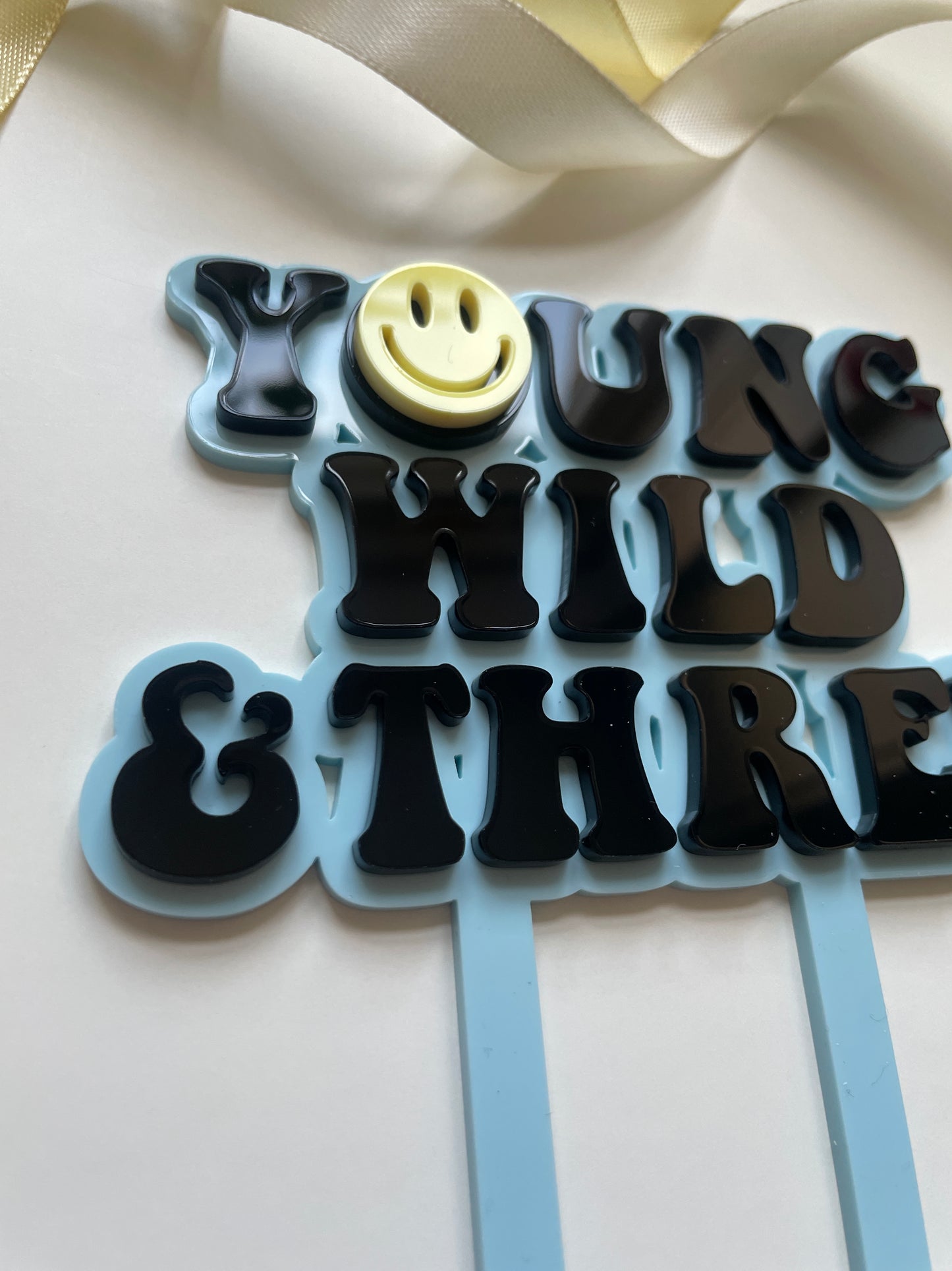 young wild and three acrylic cake topper set in blue yellow and black with lightning peace hand and smiley face charm