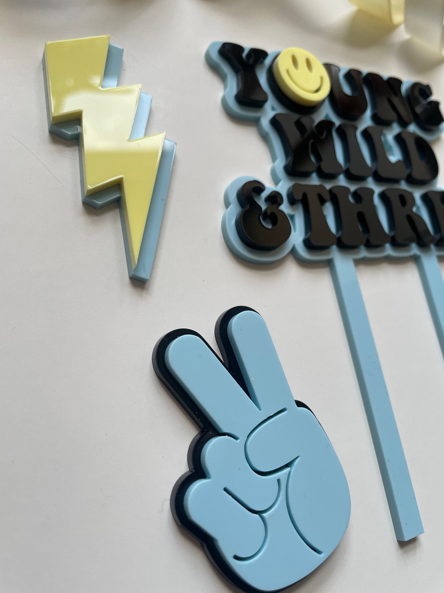 young wild and three acrylic cake topper set in blue yellow and black with lightning peace hand and smiley face charm