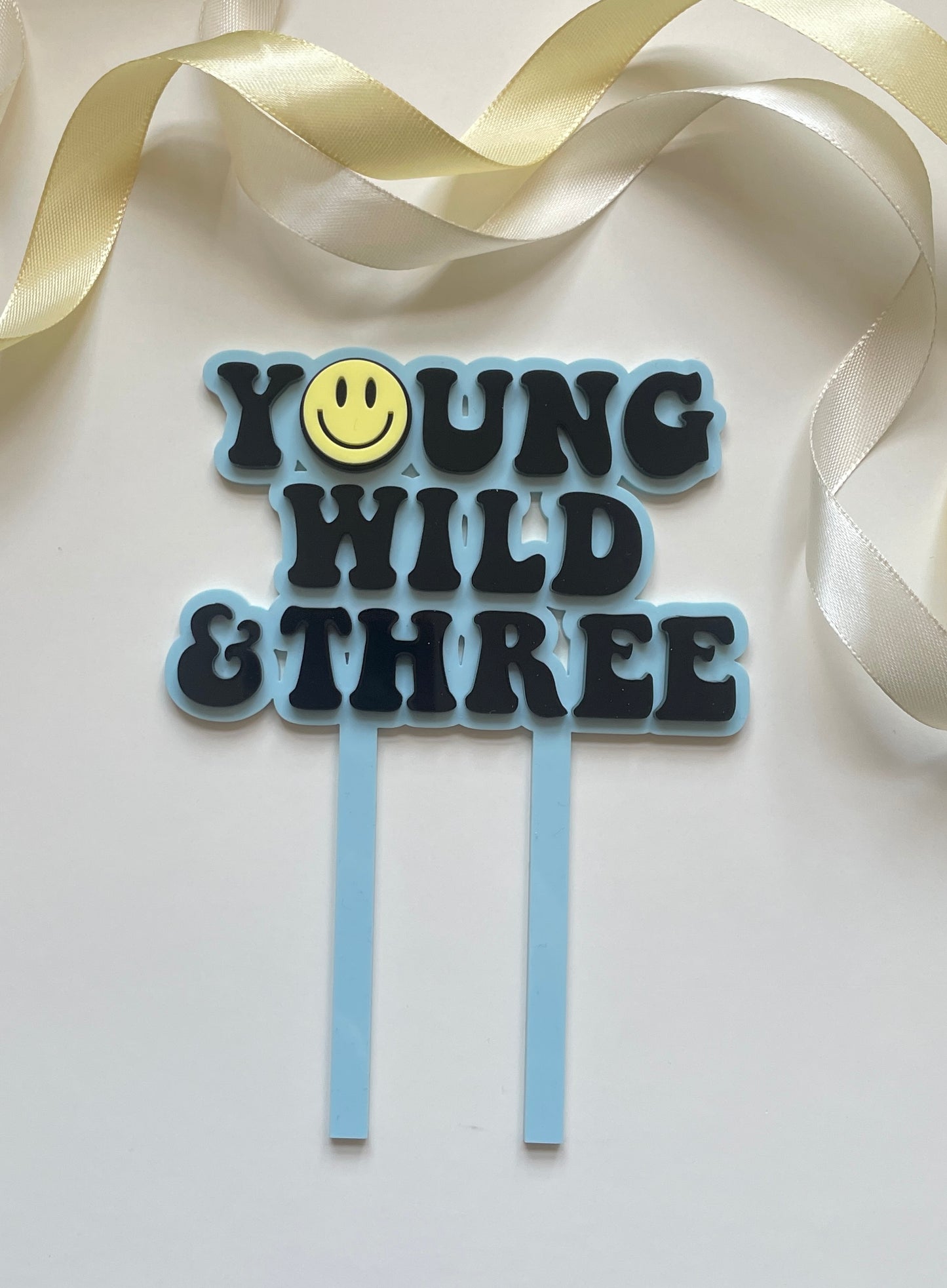 young wild and three acrylic cake topper set in blue yellow and black with lightning peace hand and smiley face charm